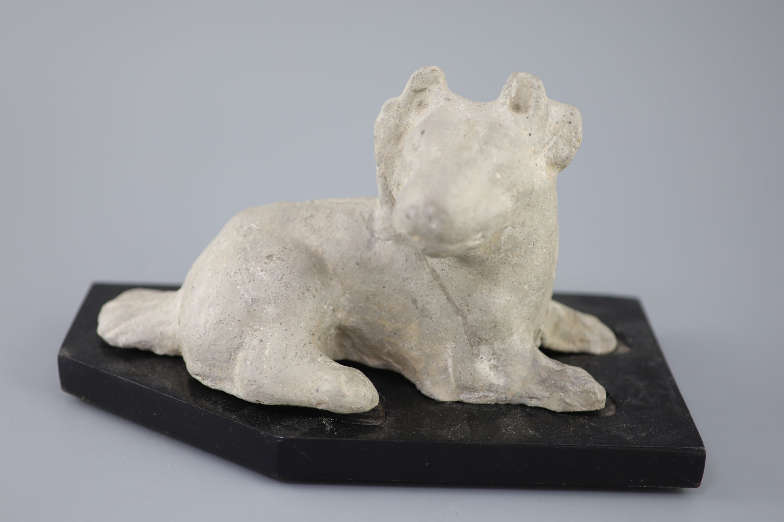 A Chinese grey pottery figure of a recumbent dog, Han dynasty or later 23.5cm long, wood stand
